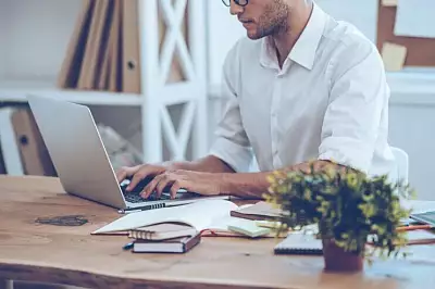 Mann am Laptop mit Taschenrechner
